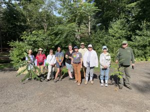 Group of volunteers standing with tree-of-heaven cutting at talk and cut event. 